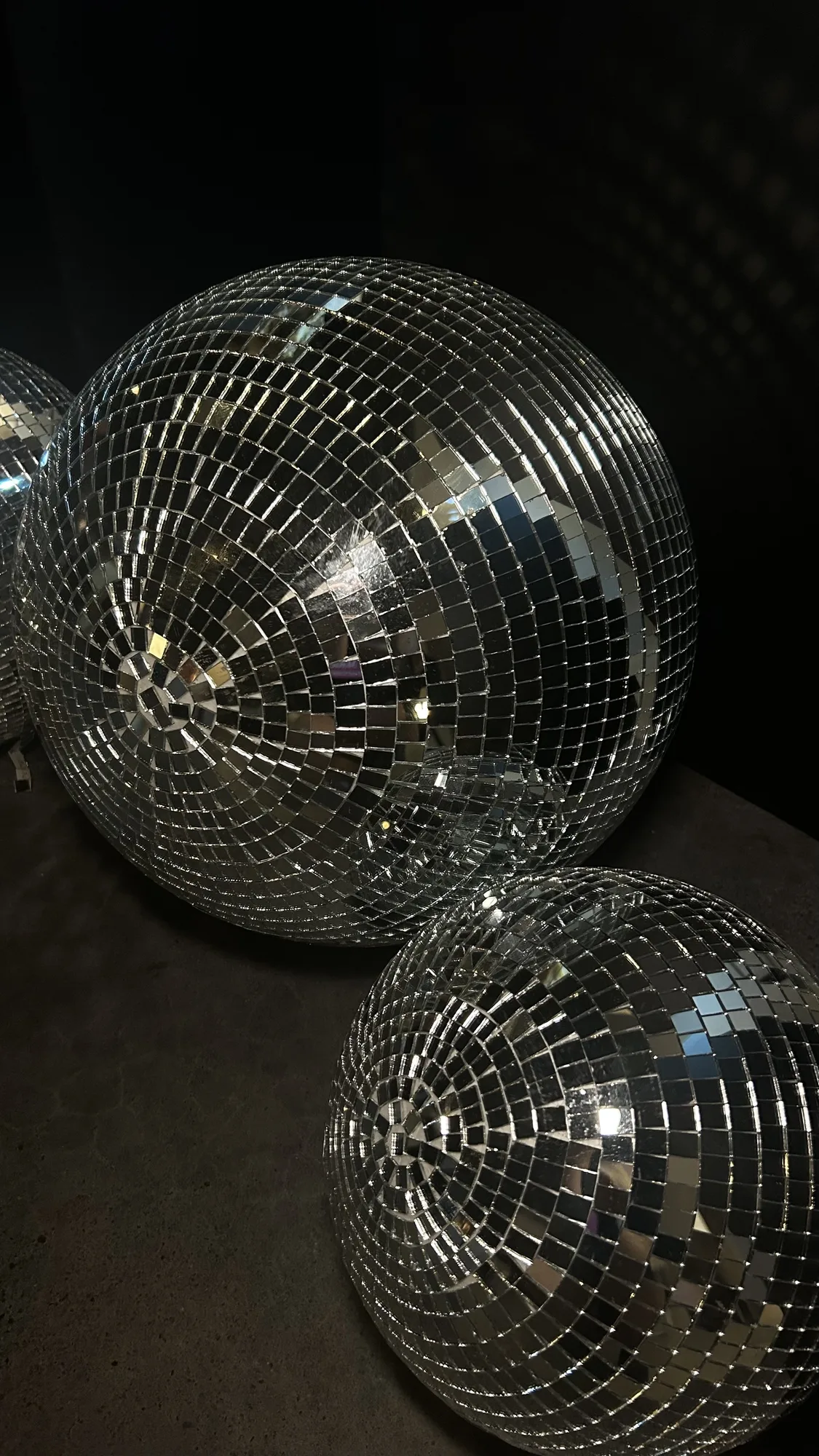 Two large mirror disco balls on a concrete surface against a dark curtain.